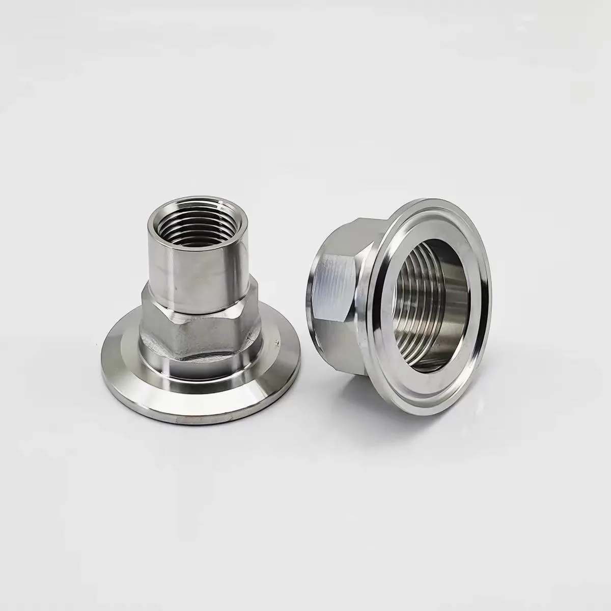 Two machined stainless steel tri-clamp adapters with sanitary ferrule flanges and internal female threads behind hex bodies
